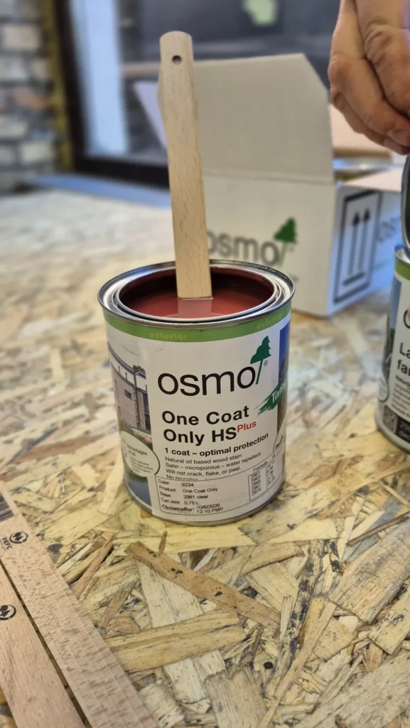 Osmo One Coat Only HS Plus (Einmal-Lasur HS Plus) kārba ar sarkanu toni uz darbagalda